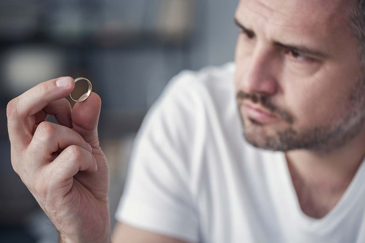 Image of a disappointed man holding a wedding ring, symbolizing the emotional weight and contemplation of ending a relationship.