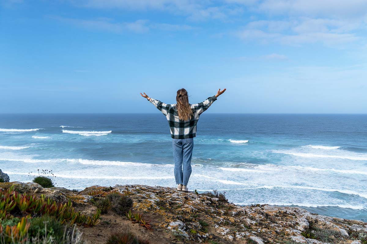 Woman in awe, practicing self-reflection on a hill overlooking the ocean