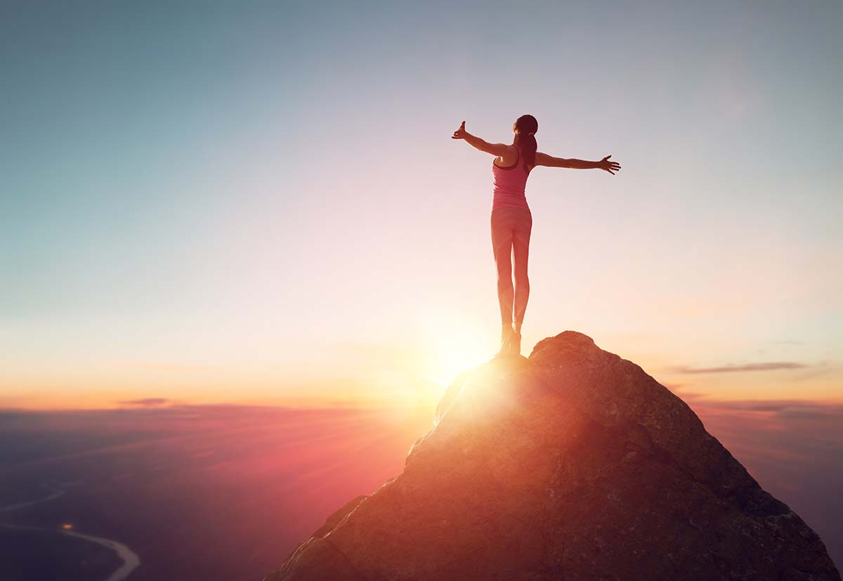 Embracing Inner Balance: Woman rejoicing atop a mountain, arms outstretched to greet the morning